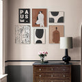 Indoor wall filled with Modern Abstract Vintage Wall Art Canvas Prints with a chest of draws in front. A vase with flowers and a light sitting on top of the chest of draws